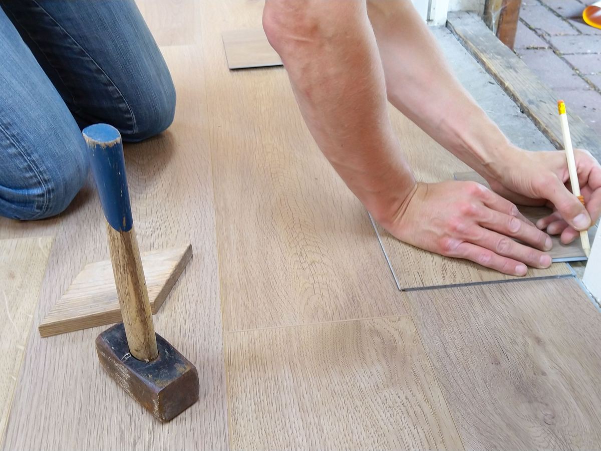 Hände verlegen Laminat, daneben Hammer und Schlagholz
